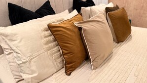 Ein Bett mit vielen Kissen, einer gemusterten Decke und einem Kopfteil.