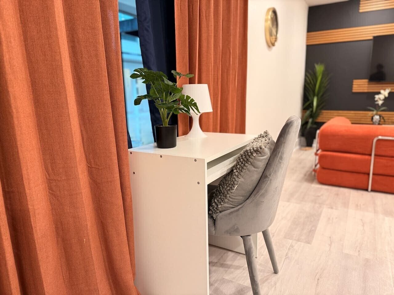 A modern living room with a white desk, a grey chair, a red sofa, and a potted plant.