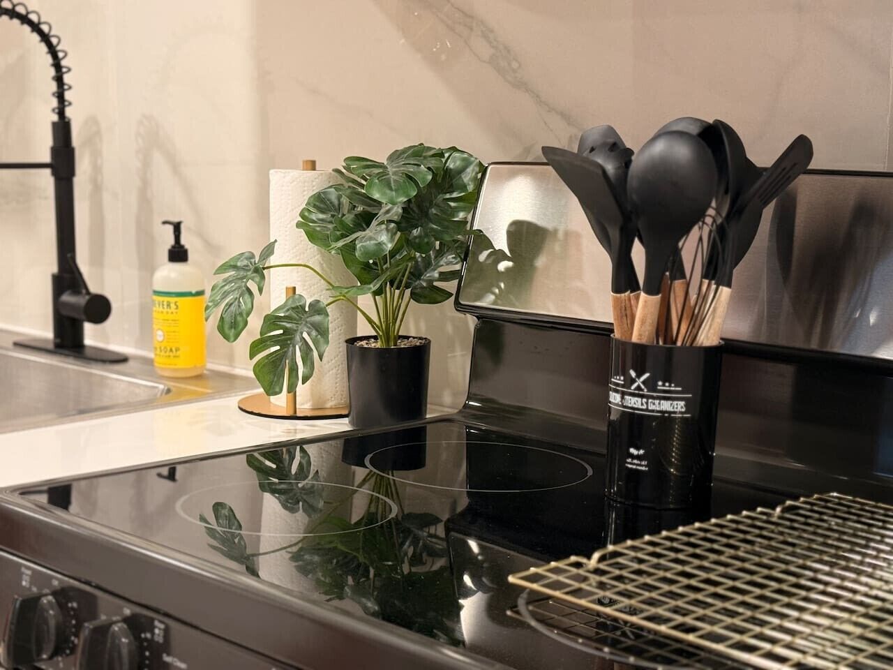 A kitchen with a black stove, a sink, a bottle of soap, and two potted plants.