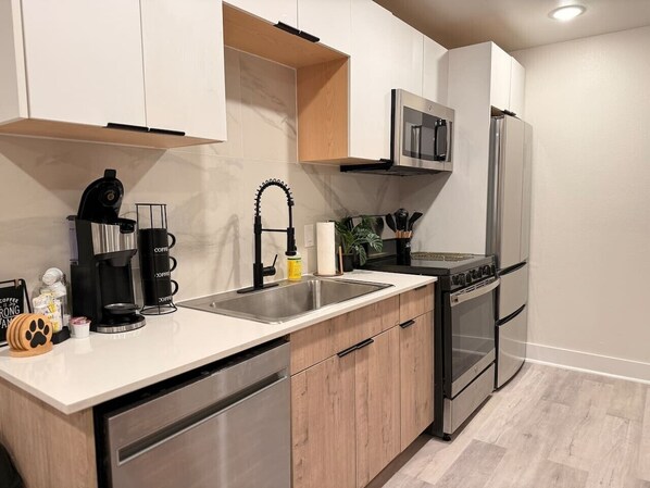A modern kitchen with a stainless steel sink, a coffee maker, a microwave, and a refrigerator. - Downtown Dallas Hideaway | Free Parking | 4 Guests (Dallas)