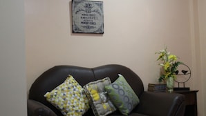 Un sofá de cuero marrón con cojines estampados, un cartel decorativo en la pared y una mesita con un florero.