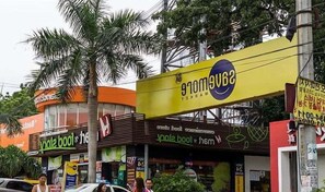 Vista de una calle con diversos comercios, incluyendo una farmacia visible y una tienda con un letrero amarillo llamativo.