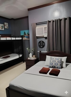 Habitación de hotel con literas, una cama individual con un reloj, una mesita de noche y una ventana con cortinas.