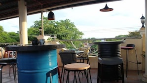 Un patio al aire libre con mesas y sillas, un barril azul grande y lámparas colgantes.