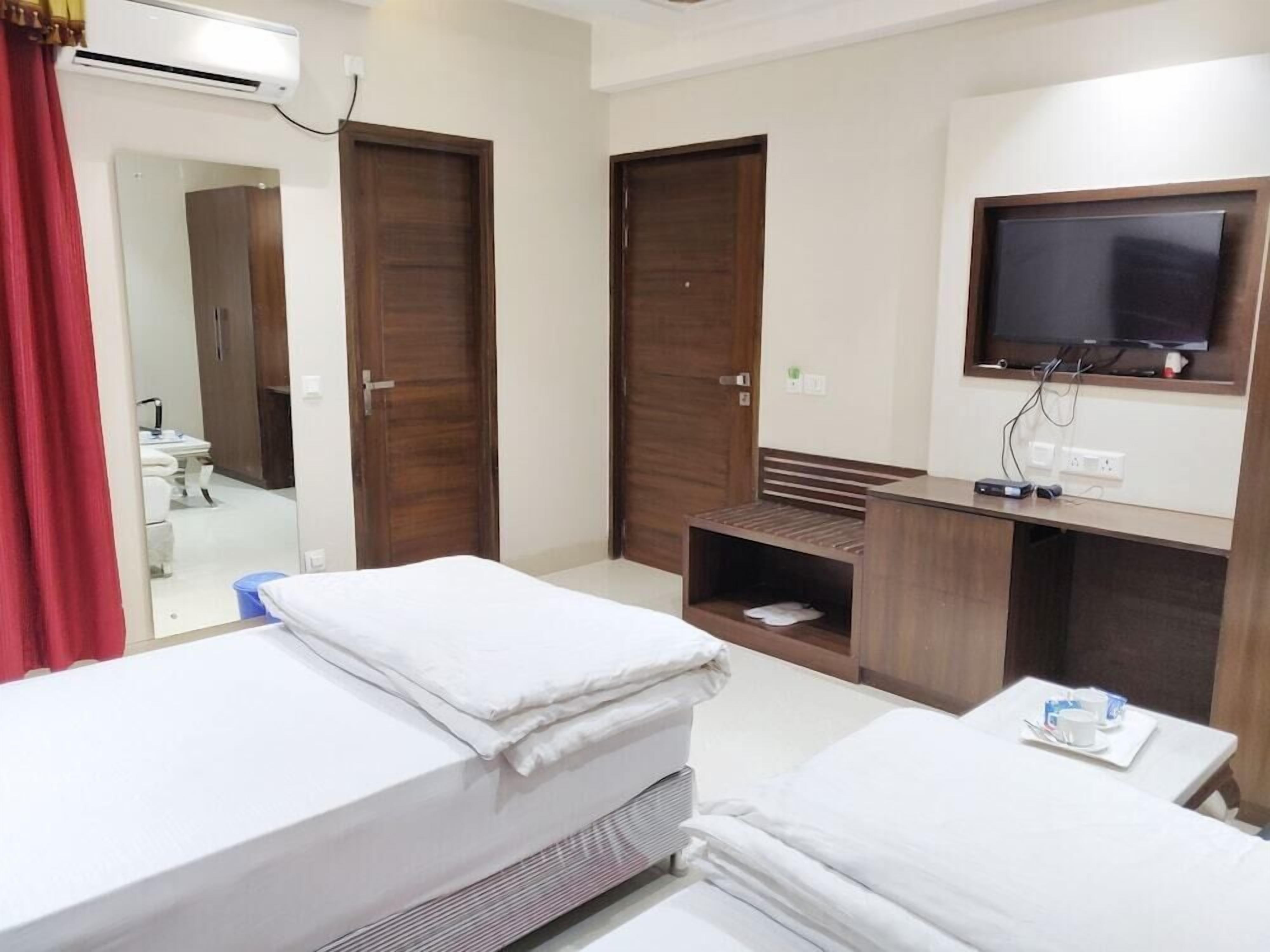A hotel room with two beds, a TV, a desk with a chair, and a bathroom visible through an open door.