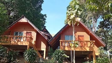 Two wooden cabins with balconies, surrounded by dense foliage and a clear sky.