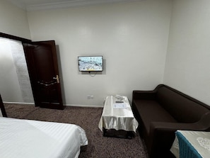 Una camera d'albergo con un letto, un tavolino con il telefono, una televisione a parete e un divano marrone.