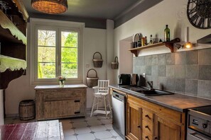 A kitchen with a wooden cabinet, a white chair, a sink, and a stove. - LES Maisons DE LEA (Honfleur)