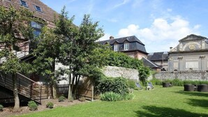 Een binnenplaats met een gazon, een stenen muur en een houten trap naar een gebouw.