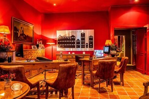 Un hall d ’hôtel aux couleurs dominantes rouges, agrémenté d’un grand tableau, d’un écran numérique et d’un espace repas avec des meubles en bois.
