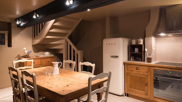 Een keuken met een houten tafel, witte stoelen, een witte koelkast en een inbouwoven.