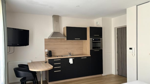 Una cocina moderna con encimera de madera, armarios negros y horno empotrado. Cuenta con un pequeño comedor con una mesa y dos sillas.