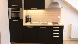 Cocina compacta con gabinetes negros, extractor de acero inoxidable, cafetera y fregadero.