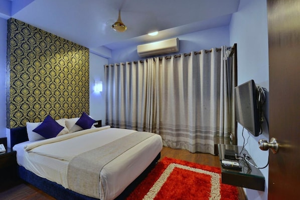 Una habitación de hotel con cama, televisión, equipo de aire acondicionado y alfombra roja.