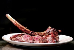 Un plato con carne cocida y un hueso, probablemente un palillo de cordero, sobre un plato blanco.