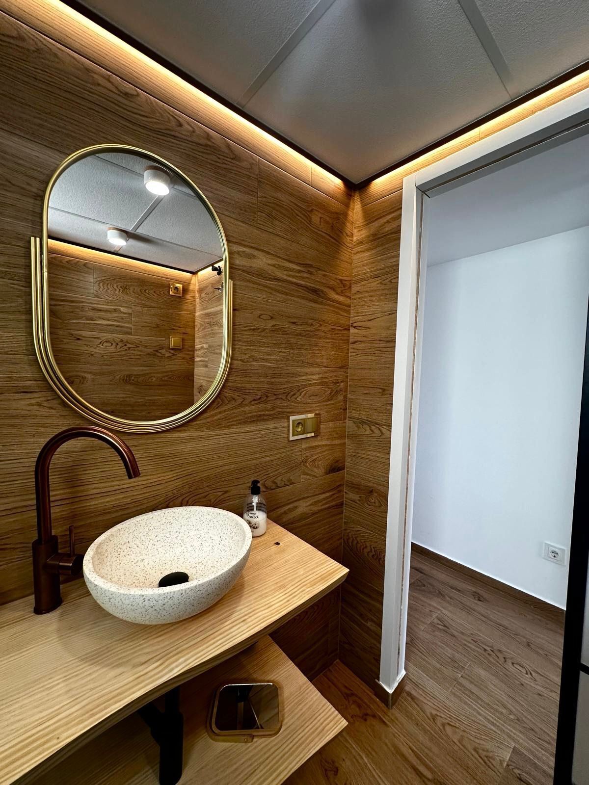 A modern bathroom with a wooden vanity, a round sink, a mirror, and a shower area.