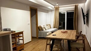 A compact living space with a wooden dining table, a sofa, and a TV mounted on the wall.