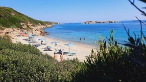 Ein Strand mit Sonnenschirmen und Liegestühlen, felsigen Klippen und klarem, blauem Wasser.