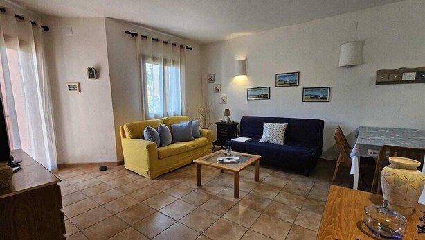 Ein Wohnzimmer mit einem gelben Sofa, einem blauen Sofa, einem Couchtisch und einem Esstisch mit Stühlen.