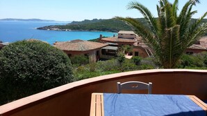 Ein Balkon mit einem Bett, mit Blick auf eine Küstenlandschaft mit Häusern und dem klaren, blauen Meer.