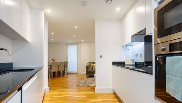 Une cuisine moderne avec un plancher en bois, des meubles blancs et des appareils électroménagers en acier inoxydable.
