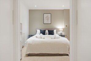 Ein ordentlich eingerichtetes Schlafzimmer mit einem großen Bett, einem Nachttisch mit Lampe und einem gerahmten Kunstwerk an der Wand.
