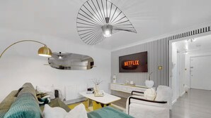 A modern living room with a sofa, a coffee table, a TV mounted on the wall, and a unique ceiling fan. - Peaceful 2BR Flat |Near Becontree Stn.|Family|ST (Greater London)