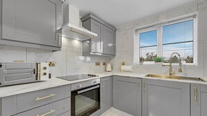 A modern kitchen with grey cabinets, a built-in oven, a stainless steel range, and a window with blinds. - Peaceful 2BR Flat |Near Becontree Stn.|Family|ST (Greater London)