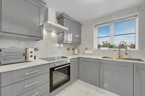 Eine moderne Küche mit grauen Schränken, einem eingebauten Backofen, einem Edelstahlherd und einem Fenster mit Jalousien.