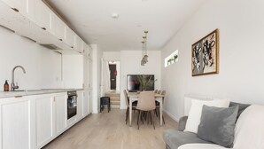 Una cucina moderna con mobili bianchi, un'area pranzo con tavolo e sedie, e un divano grigio in un soggiorno.