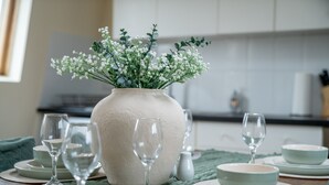 A dining table set with white plates, bowls, and wine glasses, centered around a large vase with white flowers. - Comfy & Spacious 3 BR Flat | Family |Fast Wi-Fi|ST (Greater London)