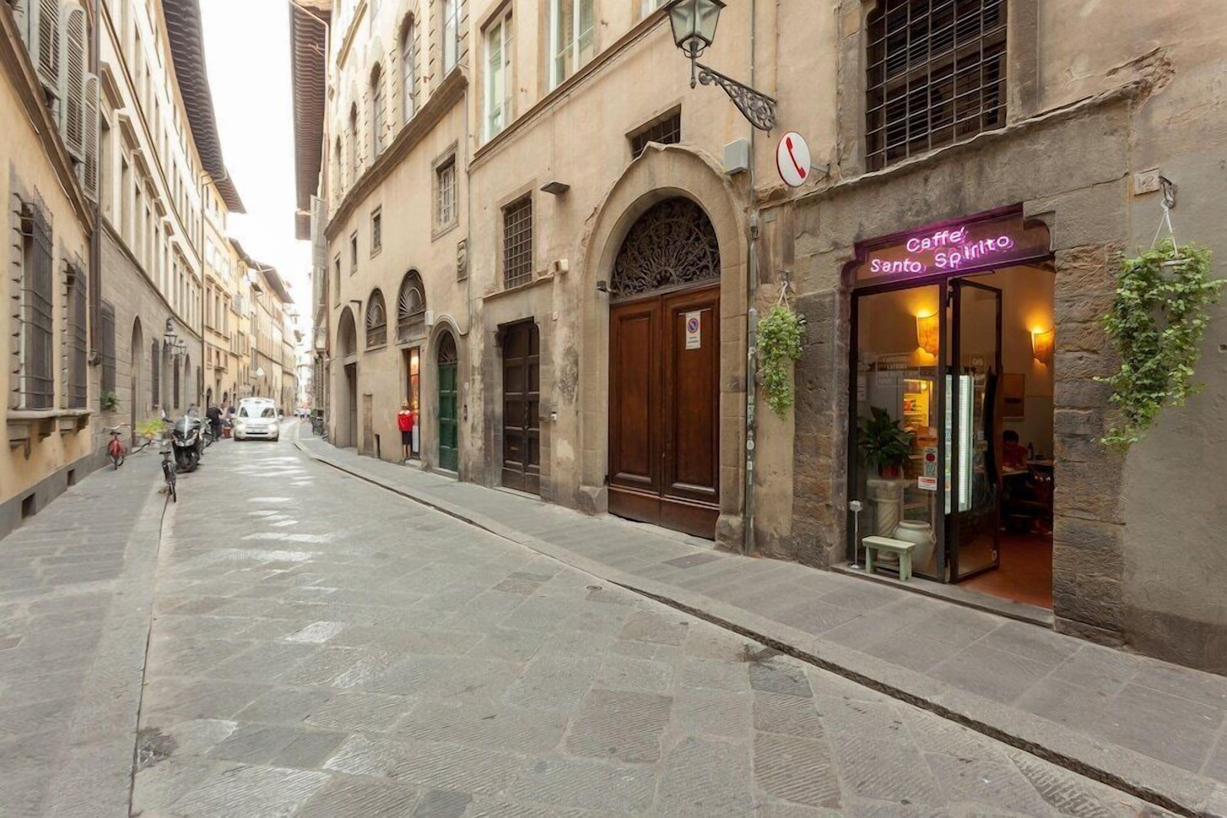 A narrow street with historic buildings, a café named 'Caffè Santo Spirito', and a closed shop with a 'No Parking' sign.