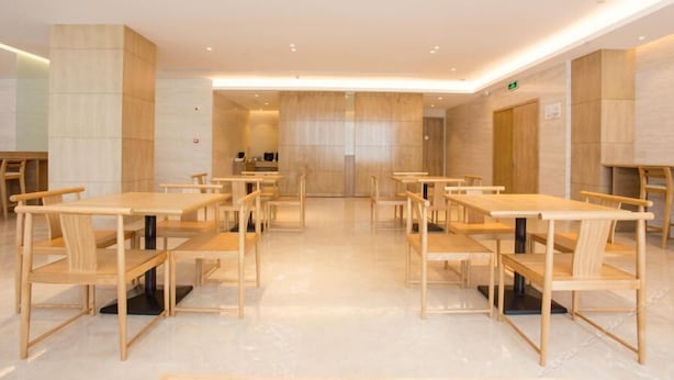 A modern dining area with wooden tables and chairs, a central service counter, and a clean, minimalist design. - Ji Hotel (Shanghai)