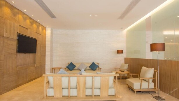 A modern hotel room with a wooden accent wall, a flat-screen TV, a sofa with cushions, a floor lamp, and a small table. - Ji Hotel (Shanghai)