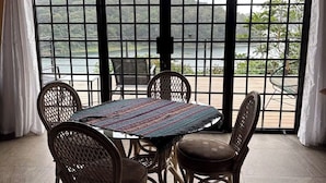 Ein Essbereich mit einem runden Tisch und Korbstühlen, großen Fenstern mit Seeblick und Grünflächen, sowie einer Decke mit sichtbaren Balken.