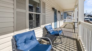En inglasad veranda med två blå, vadderade stolar och ett litet bord, träräcken och utsikt över gatan.
