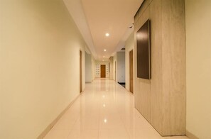Un pasillo moderno de hotel con suelo pulido, paneles de madera y luces empotradas en el techo.