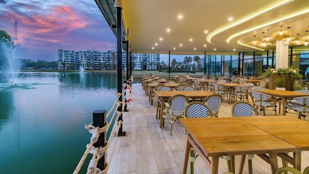 Un restaurant en plein air, avec des tables et des chaises, offrant une vue sur un plan d’eau et un ciel au coucher du soleil.