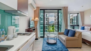 Une chambre d’hôtel moderne équipée d’une kitchenette, d’un canapé, d’un lit et d’une grande fenêtre offrant une vue sur les bâtiments et les montagnes.