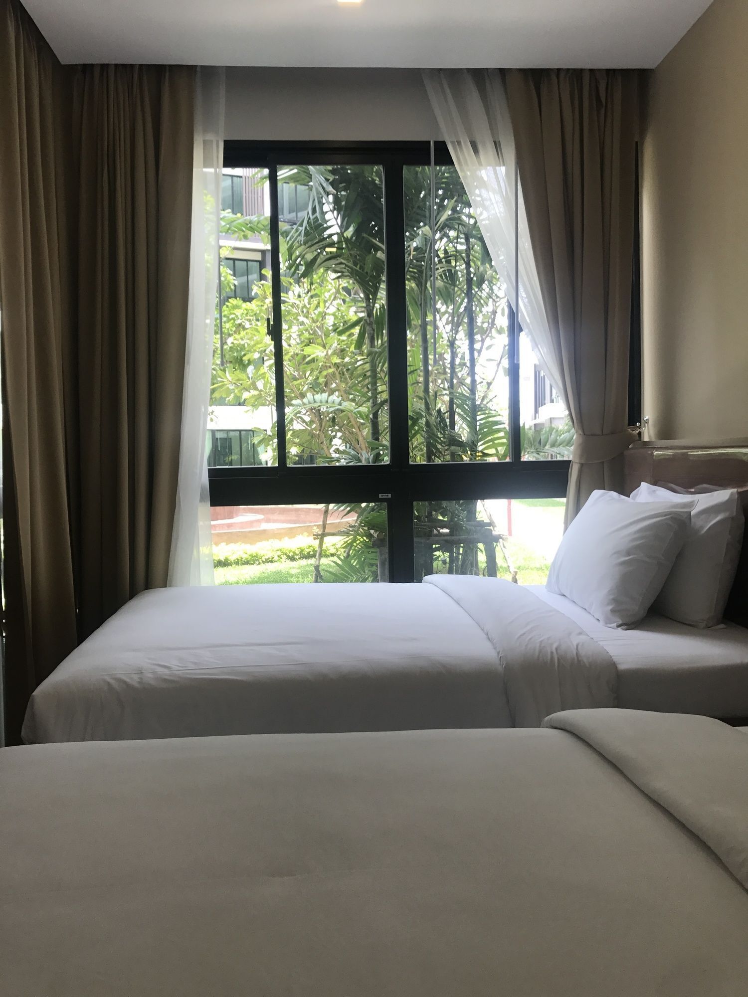 A hotel room with a large window, a bed with white linens, and a view of greenery outside.
