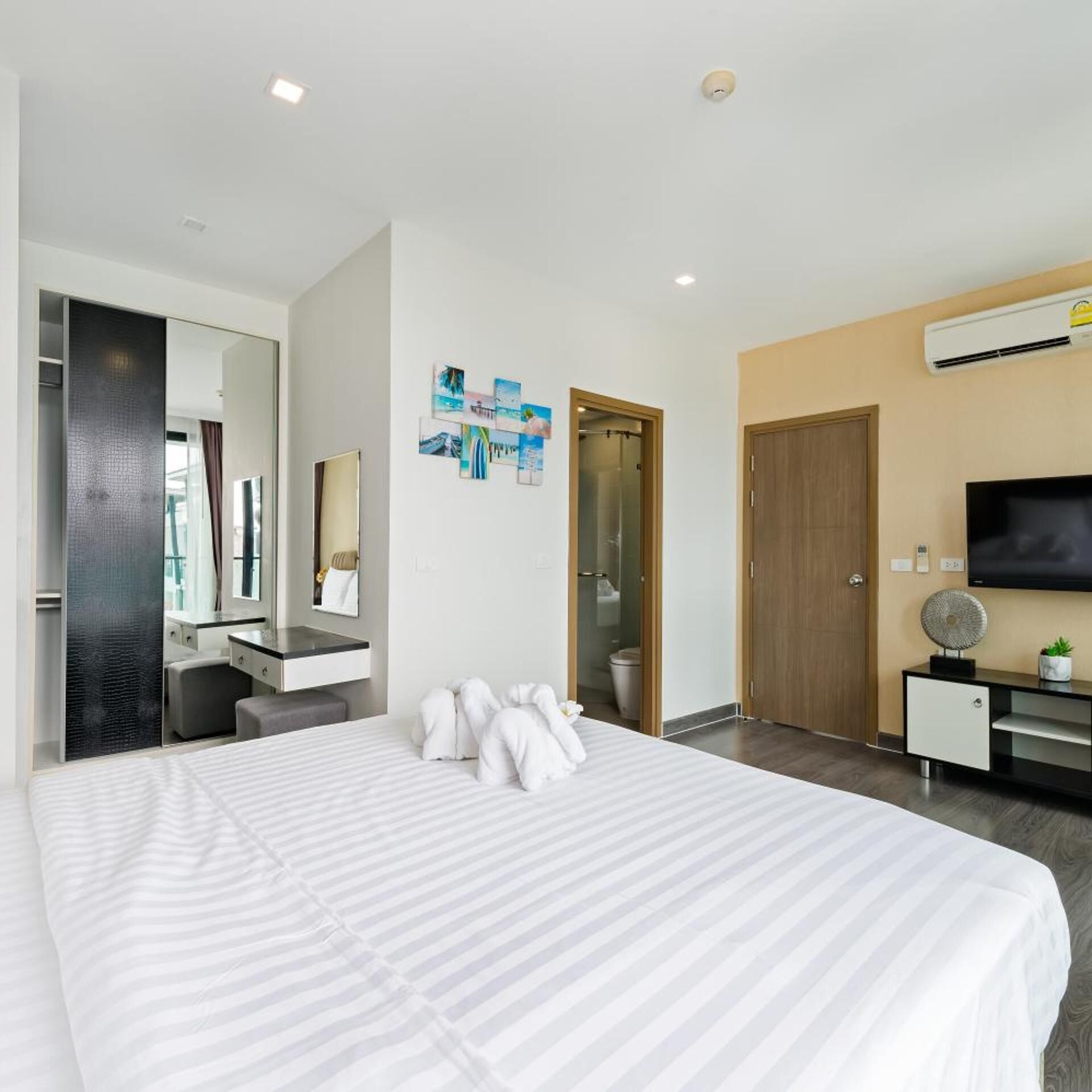 Una habitación de hotel moderna con una cama grande, un baño con puerta de vidrio, un televisor de pantalla plana y un escritorio pequeño.