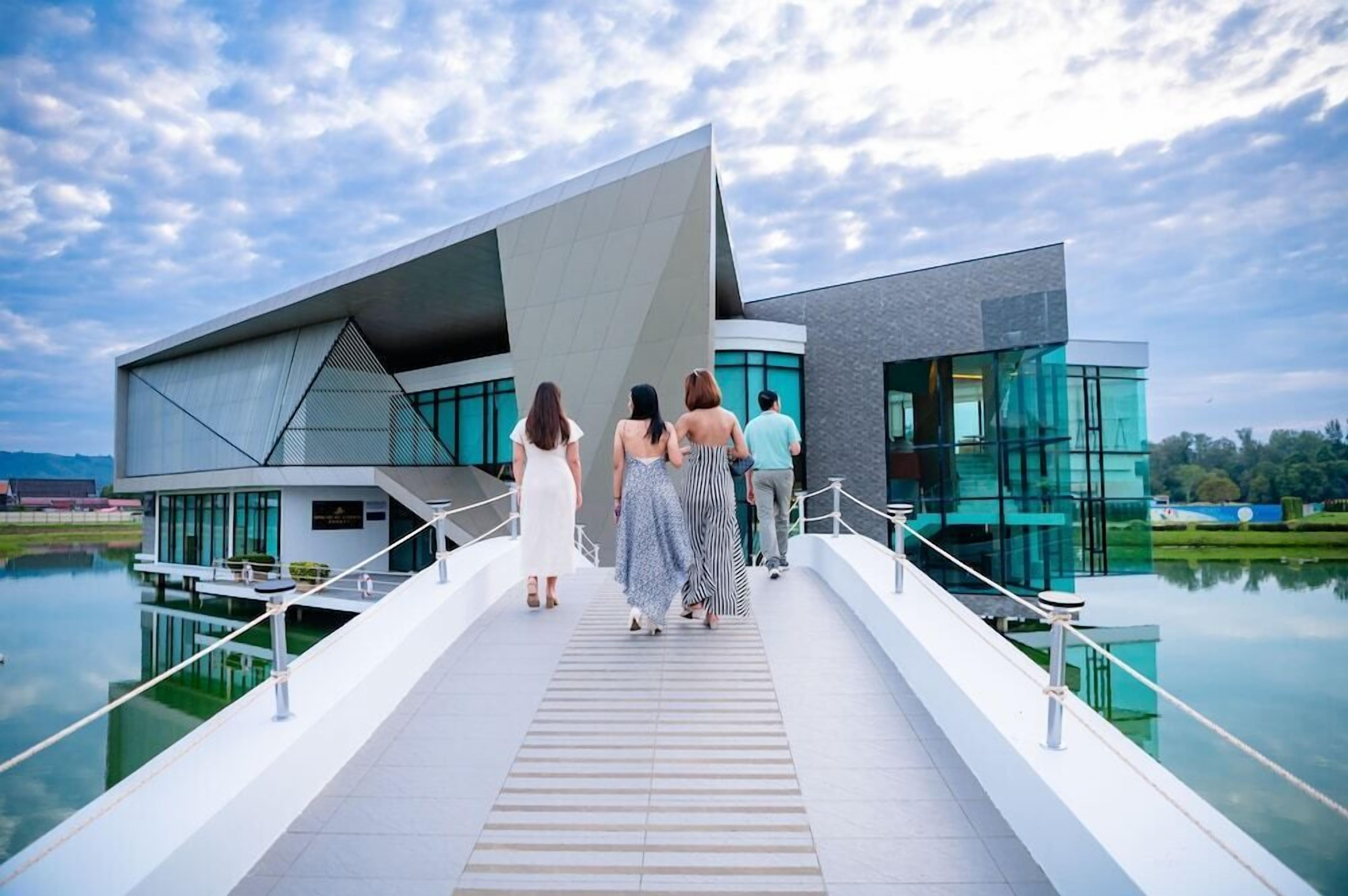 A modern building with a unique architectural design, featuring a large glass facade and a reflective water body in front.