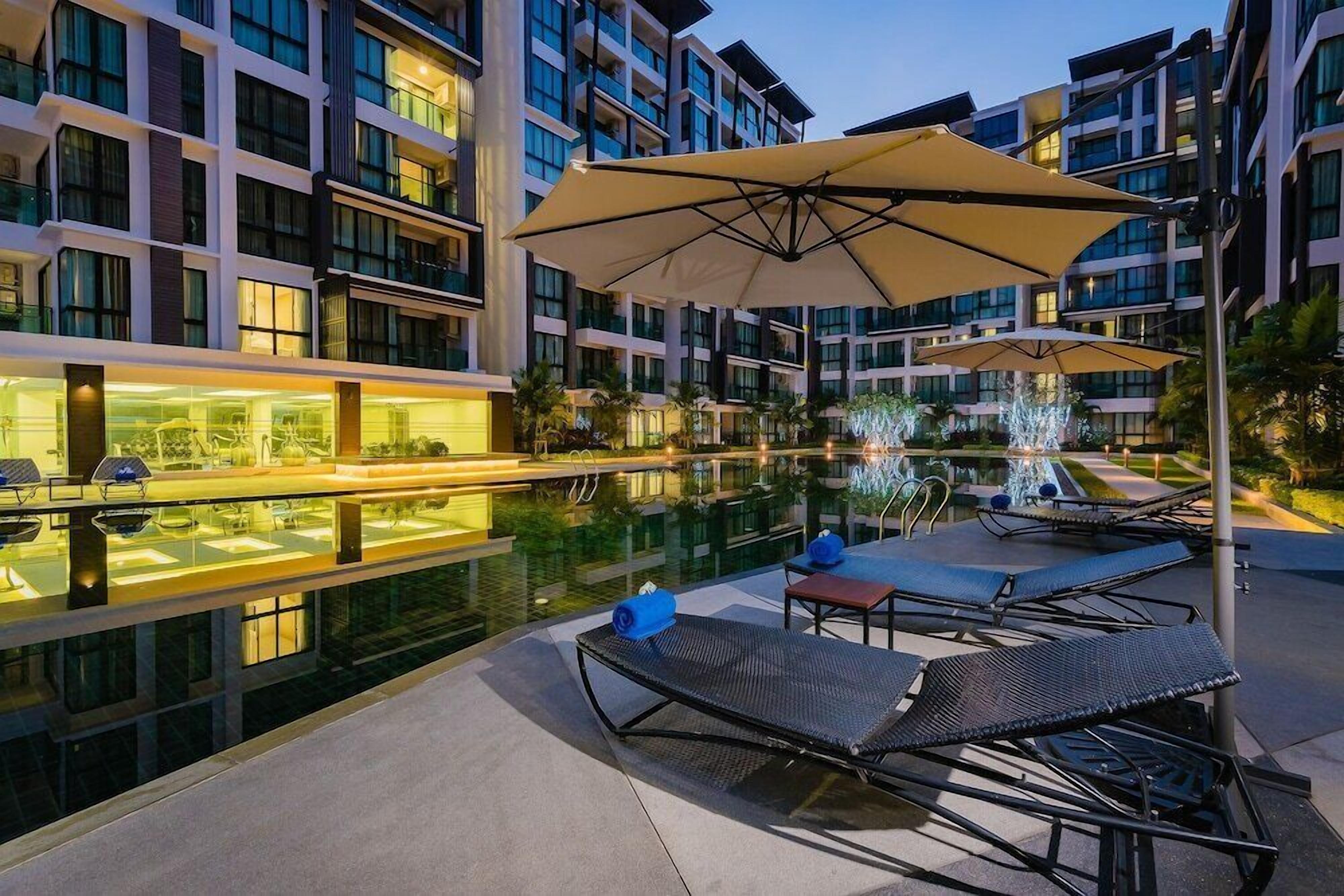 A modern hotel pool area with lounge chairs, umbrellas, and a glass-enclosed spa area.