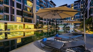 Un espace piscine moderne avec des chaises longues, des parasols et un espace spa fermé par des parois de verre.