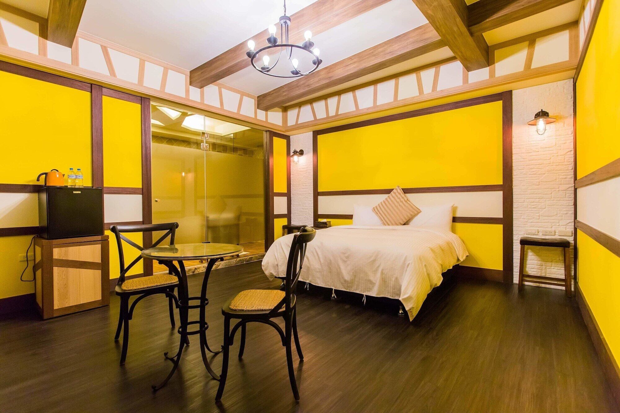 A room with a bed, two chairs, a small table, a TV, and a glass partition.