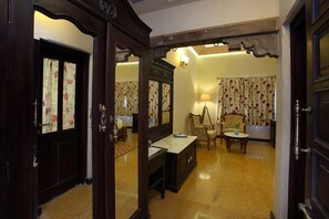 Habitació tradicional amb sòl de fusta, escriptori, dues cadires, làmpada i cortines amb motius florals.
