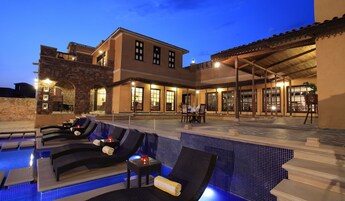 Zona de piscina con sillones de descanso y un patio cubierto con mesas y sillas.
