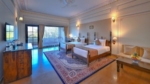 A spacious bedroom with two large beds, a wooden desk, and a seating area with a sofa. - The Tigress Spa and Resort (Sawai Madhopur)