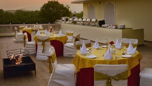 A banquet setup with round tables, white and gold chairs, and a buffet table. - The Tigress Spa and Resort (Sawai Madhopur)