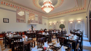 A dining area with multiple tables set for service, a chandelier, and ornate wall decorations. - The Tigress Spa and Resort (Sawai Madhopur)